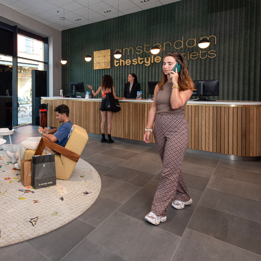 Amsterdam The Style Outlets servicepunt , vrouw aan het bellen, groene muur, jongen aan het zitten